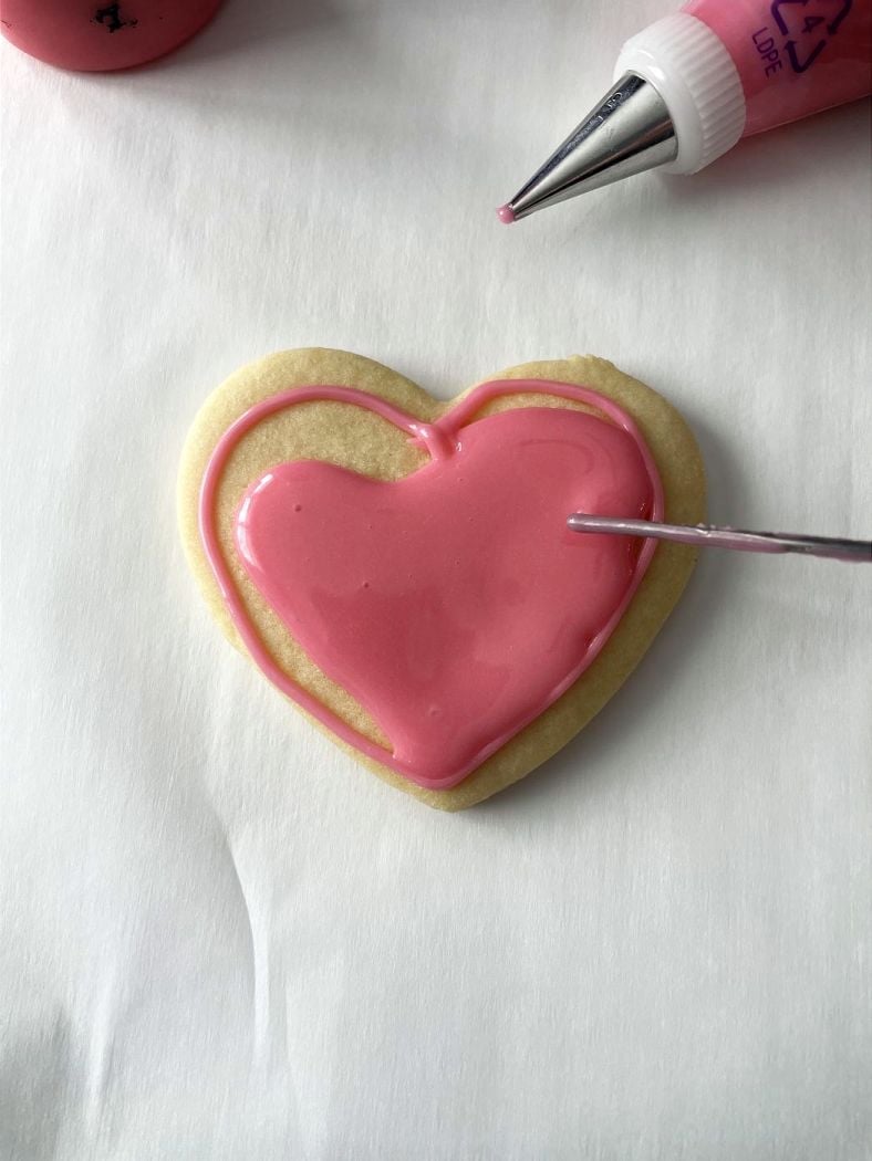 heart cookie being frosted with pink royal icing